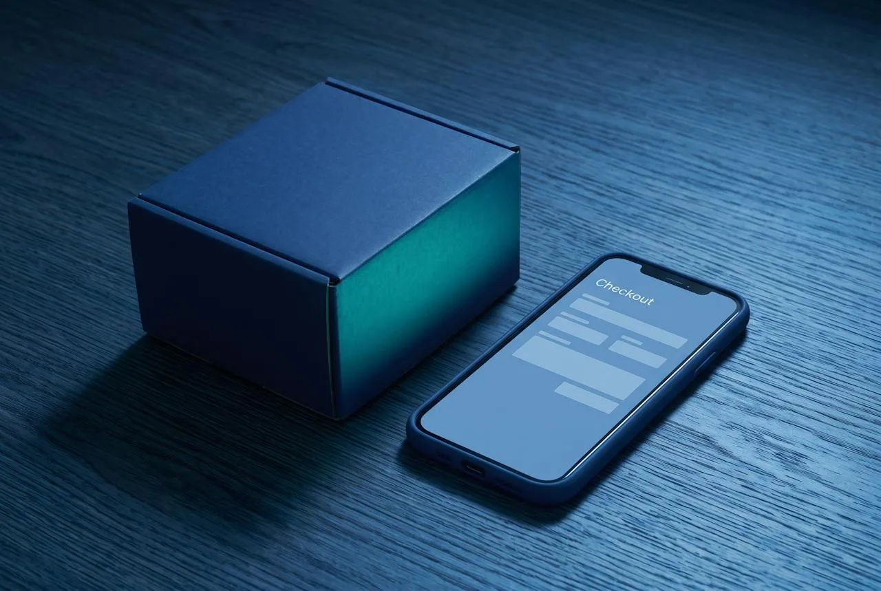 Shipping box and a smartphone showing a checkout screen on a dark desk